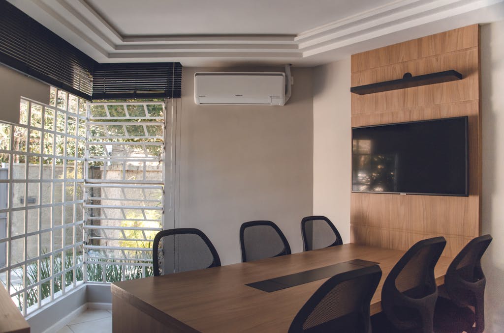 Spacious modern conference room featuring wooden table, chairs, TV, and air conditioning unit.
